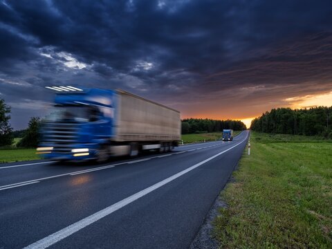 Motion blurred blue trucks driving on asphalt road in rural landscape at sunset