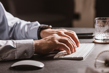 Close-up of a man’s hands using a wireless mouse and keyboard at a modern office desk. Business...