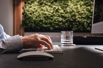 Close-up of a man’s hands using a wireless mouse and keyboard at a modern office desk. Business and remote work concept with minimalist workspace and professional atmosphere.