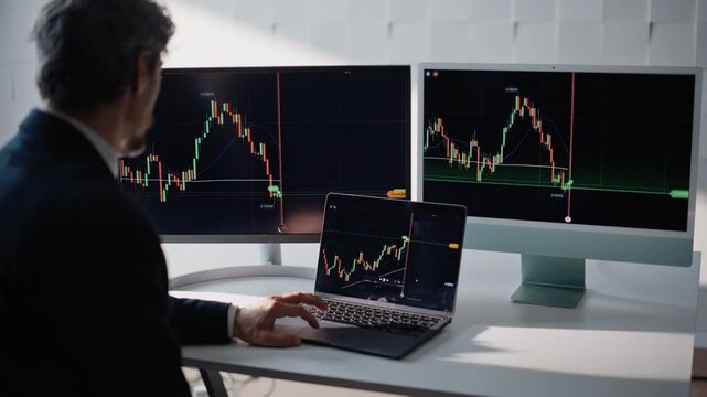 Crypto trader analyzing stock charts on laptop at office over shoulder view