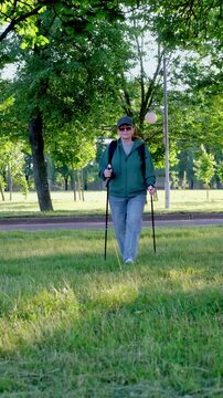 Active woman doing Nordic walking in city park, sporty outfit, using walking poles, healthy lifestyle and outdoor exercise, 4K UHD stock footage vertical frame