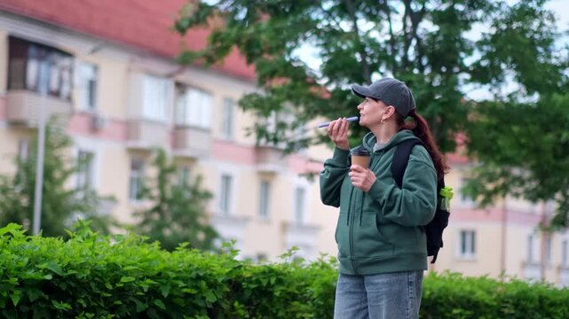 Sporty smiling woman enjoying coffee while talking on smartphone against urban background. Relaxed and happy mood in 4K lifestyle footage.