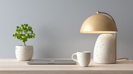 Fototapeta premium Minimalist workspace with a small potted plant, a closed laptop, a ceramic mug, and a modern beige desk lamp on a light wooden surface against a gray wall.