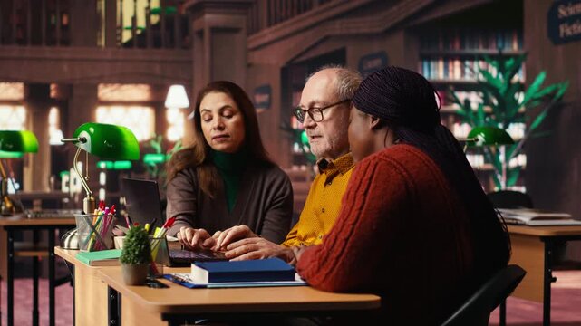 Multiethnic group of students discussing about academic materials, reading and doing research for upcoming exams. Diverse people showing commitment for personal growth. Camera B.