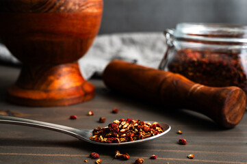 Spoonful of Crushed Szechuan Peppercorns Close-up: Crushed sichuan pepper with a mortar and pestle  and spice jar in the background