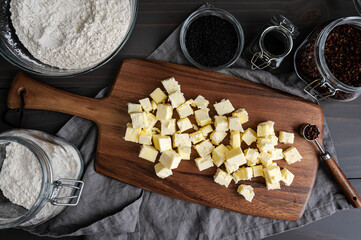 Cubed Butter on a Wooden Cutting Board with Spices and Flour: Cubes of butter with jars of flour, black sesame seeds, and Szechuan peppercorns