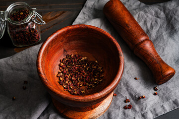 Crushed Szechuan Peppercorns in a Wooden Mortar and Pestle: Cracked Sichuan pepper in a rustic mortar with a small jar of whole peppercorns