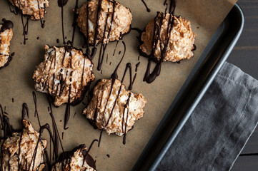 Macaroons Drizzled with Dark Chocolate on a Sheet Pan Close-up: Coconut meringue drop cookies dipped in bittersweet chocolate on parchment paper