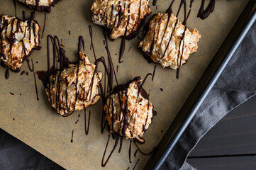 Macaroons Drizzled with Dark Chocolate on a Sheet Pan Close-up: Coconut meringue drop cookies dipped in bittersweet chocolate on parchment paper