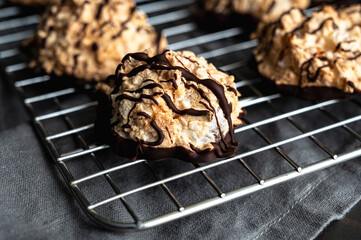 Macaroons Drizzled with Dark Chocolate on a Wire Rack Close-up: Coconut meringue drop cookies dipped in bittersweet chocolate on a cooling rack
