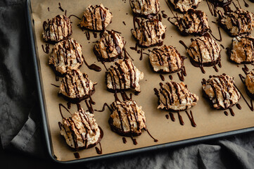 Macaroons Drizzled with Dark Chocolate on a Sheet Pan Close-up: Coconut meringue drop cookies dipped in bittersweet chocolate on parchment paper