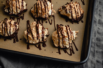 Macaroons Drizzled with Dark Chocolate on a Sheet Pan Close-up: Coconut meringue drop cookies dipped in bittersweet chocolate on parchment paper