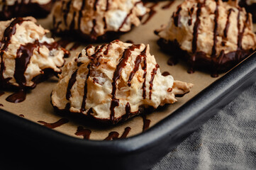 Macaroons Drizzled with Dark Chocolate on a Sheet Pan Close-up: Coconut meringue drop cookies dipped in bittersweet chocolate on parchment paper