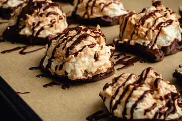 Macaroons Drizzled with Dark Chocolate on a Sheet Pan Close-up: Coconut meringue drop cookies dipped in bittersweet chocolate on parchment paper