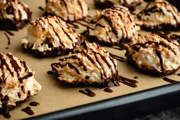 Macaroons Drizzled with Dark Chocolate on a Sheet Pan Close-up: Coconut meringue drop cookies dipped in bittersweet chocolate on parchment paper