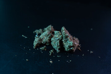 Cannabis nug on dark surface, illuminated by colored light that highlights its texture and color....