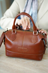 A woman's hand in formal attire is opening a brown leather bag