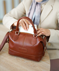 A woman's body wearing a hijab and formal attire puts her gadget into a brown leather bag.
