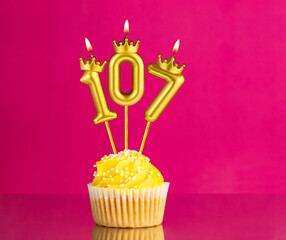 Birthday celebration with number 107 candle - Yellow cupcake on a pink background