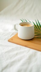 Stock photo of coffee cup on wooden tray with palm leaf on white bed sheets indoor