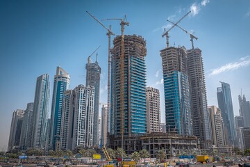 Fototapeta premium A modern city with tall buildings under construction, cranes, and concrete, set against a bright blue sky and daylight. This landscape photography captures the dynamic urban environment