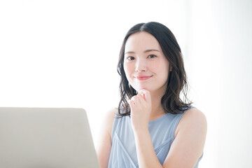 パソコンの前のかわいいカメラ目線の女性　春夏のノースリーブ白バック...
