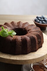 Tasty chocolate bundt cake with mint and blueberries on wooden table, closeup