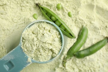 Measuring spoon and fresh pea pods on protein powder, flat lay