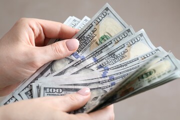 Woman counting dollar banknotes on beige background, closeup