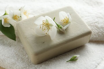 Soap bar and jasmine flowers on towel, closeup