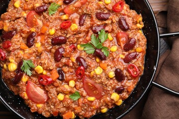 Tasty chili con carne in baking dish on wooden table, top view