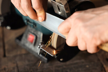 Man sharpening knife with bench grinder indoors, closeup