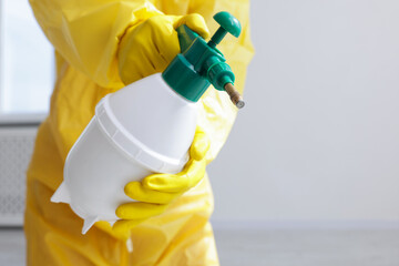 Pest control worker in protective suit spraying insecticide indoors, closeup