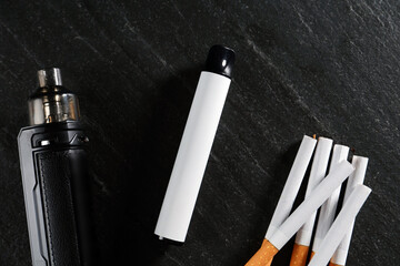Electronic smoking devices and cigarettes on black table, flat lay