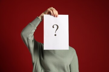 Anonymity. Woman hiding behind paper sheet with question mark on dark red background