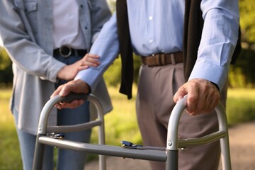 Caregiver supporting elderly man who using walking frame outdoors, closeup