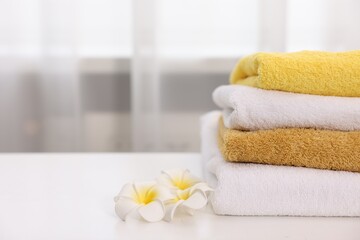 Stack of colorful towels and plumeria flowers on white table indoors, closeup. Space for text