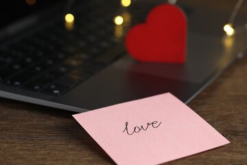 Sticky note with word Love, decorative heart and laptop on wooden table, closeup. Online dating site
