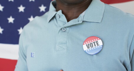 Displaying man wearing light blue polo shirt at campaign event, with VOTE button and flag backdrop