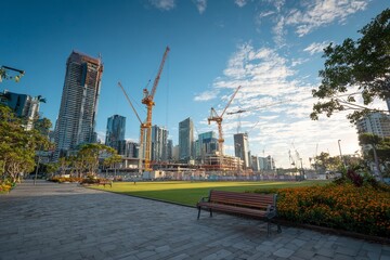city square under construction with modern high-rise buildings and cranes, symbolizing the growth of urban development. The scene is illuminated by natural sunlight against a blue sky background. Phot