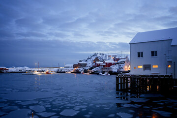 A picturesque winter harbor scene featuring snowcovered houses and icy waters all around