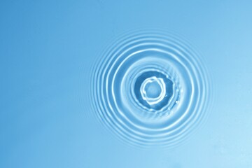 Water drops falling on blue clear water surface with circle waves, rings, texture, ripples, splash. Abstract nature banner background transparent  shining clear water, copy space, top view.