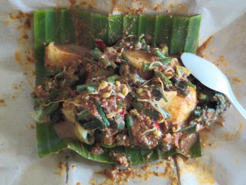 Traditional Indonesian pecel dish served on banana leaf with vegetables and spicy peanut sauce.