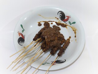 Beef satay served on skewers with rich peanut sauce in a rooster-patterned plate.