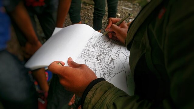 Defocused of a person sketching a detailed outdoor scene in a notebook using a pen.