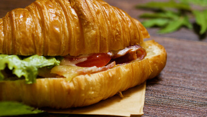 Freshly baked croissant overflowing with crispy bacon, vibrant lettuce, juicy tomato slices, and creamy cheese, offering a deliciously satisfying meal perfect for any time of day