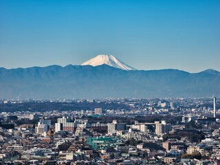 雪を戴いた冬の富士山と東京・世田谷区から望む大都市の街並み　手前の山並みは丹沢山塊