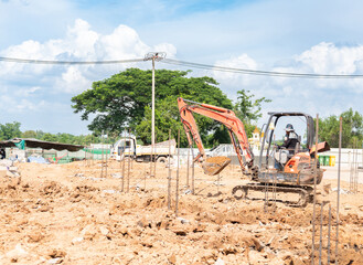A mini excavator is leveling the ground in preparation for pile driving.