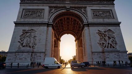 Low-angle video shot of the Arc de Triomphe at sunset, capturing cars passing by and the intricate carvings in warm, golden light.