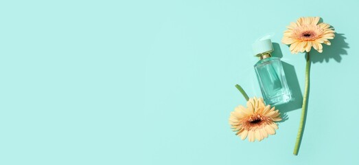 Bottle of perfume and gerberas on turquoise background with space for text, top view